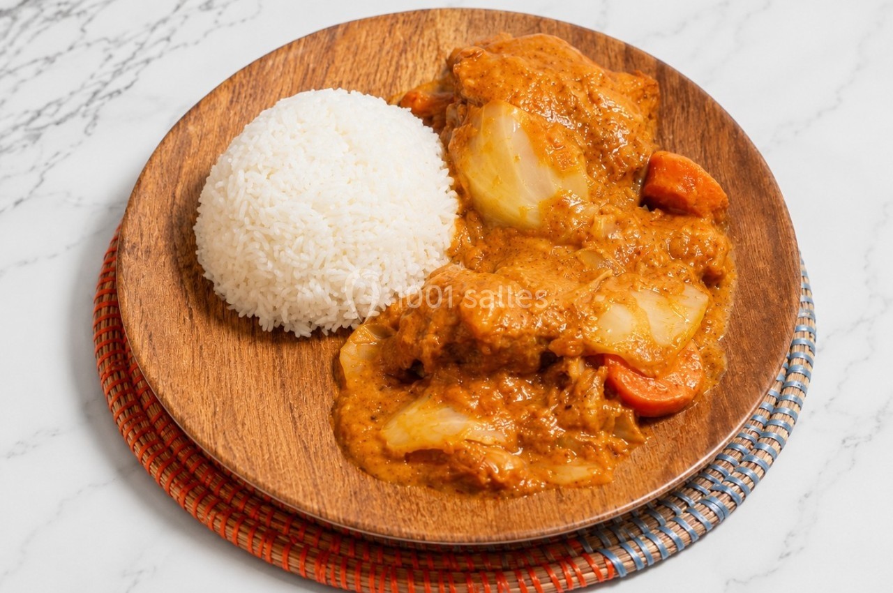 Assiette en bois contenant du riz blanc et un curry de légumes et viande avec une sauce épaisse.
