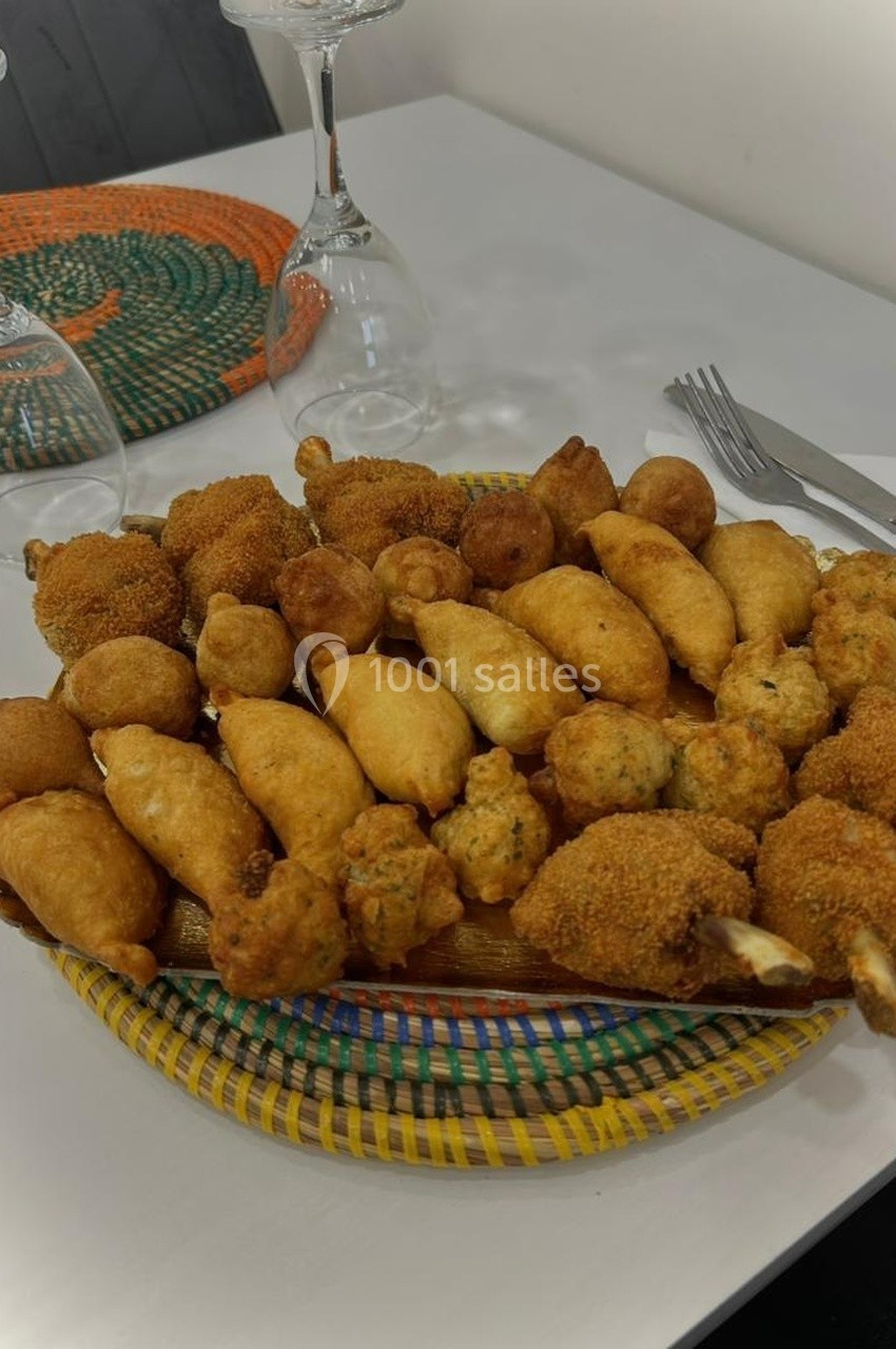 Assortiment de beignets et bouchées frits disposés sur un plateau en osier, avec des couverts et verres en arrière-plan.