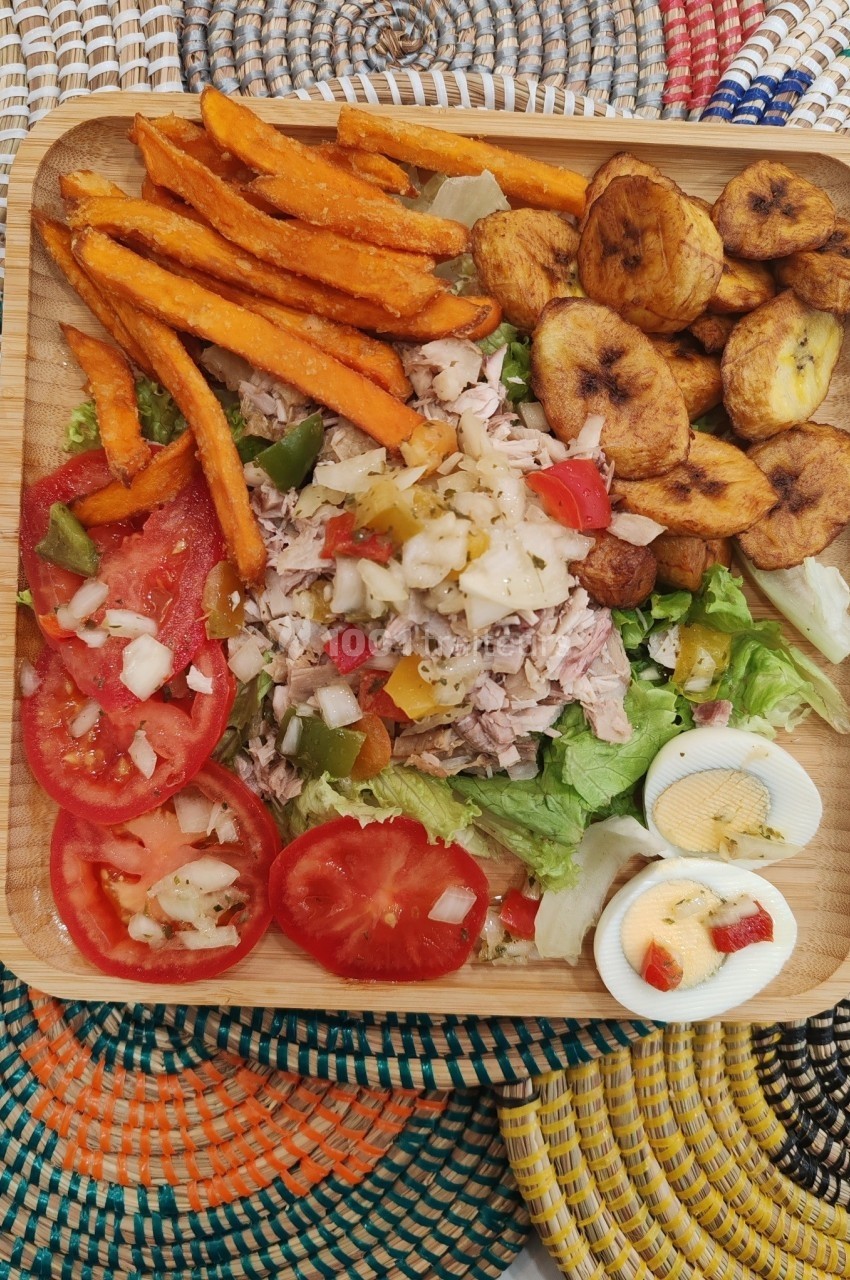 Assiette en bois contenant une salade composée, tomates, œufs durs, patates douces frites et bananes plantains grillées.