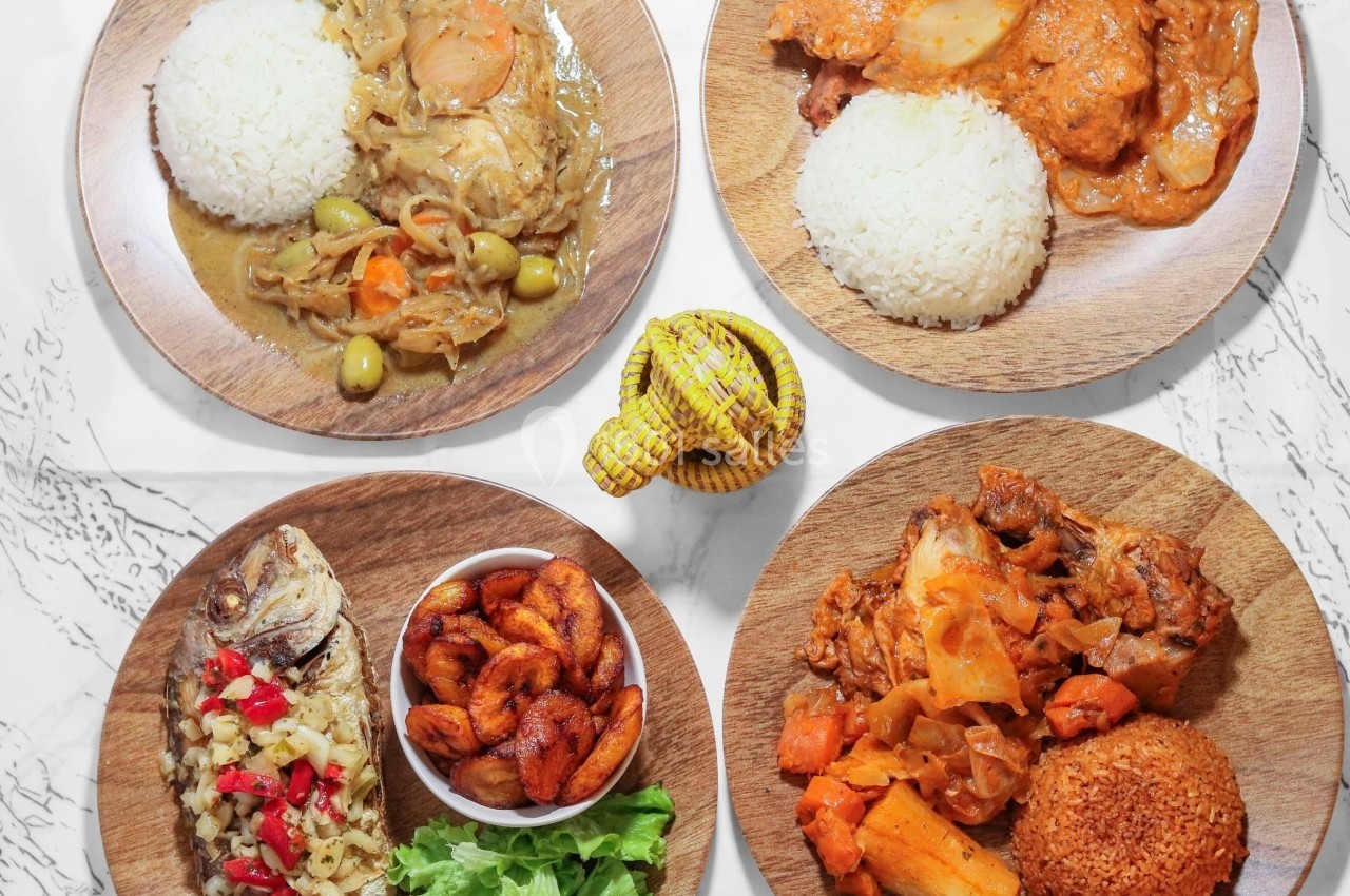 Assiettes variées de plats africains avec riz, bananes plantains, poisson, légumes et sauce, disposées sur une table.
