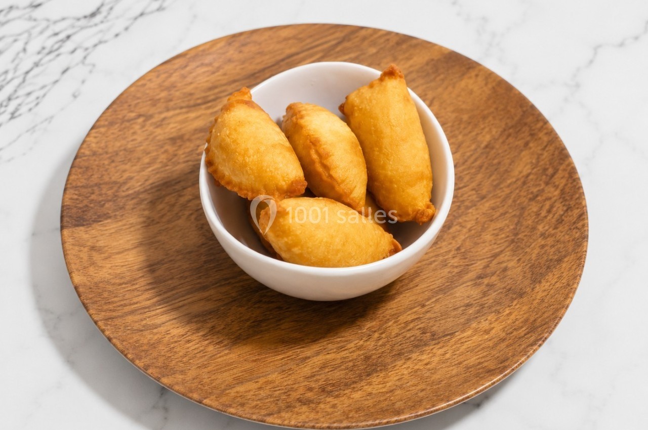 Assiette en bois contenant un bol blanc rempli de petits beignets dorés, posée sur une table en marbre.