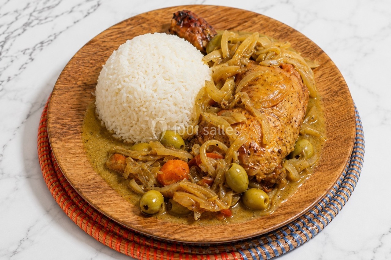 Assiette en bois contenant du riz blanc, un morceau de poulet en sauce avec olives, oignons et légumes, sur une table en…