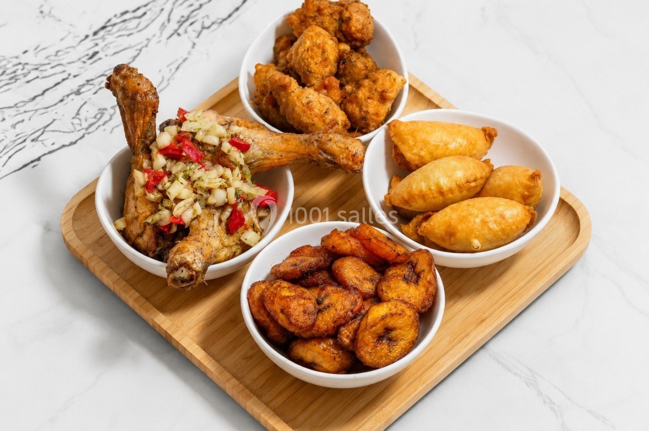 Plateau en bois avec quatre bols contenant du poulet épicé, des beignets, des empanadas et des bananes plantains frites.