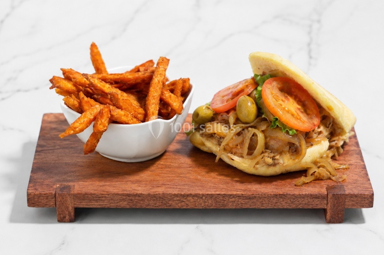 Sandwich garni de poulet, tomates, olives et oignons avec des frites de patate douce, présenté sur une planche en bois.