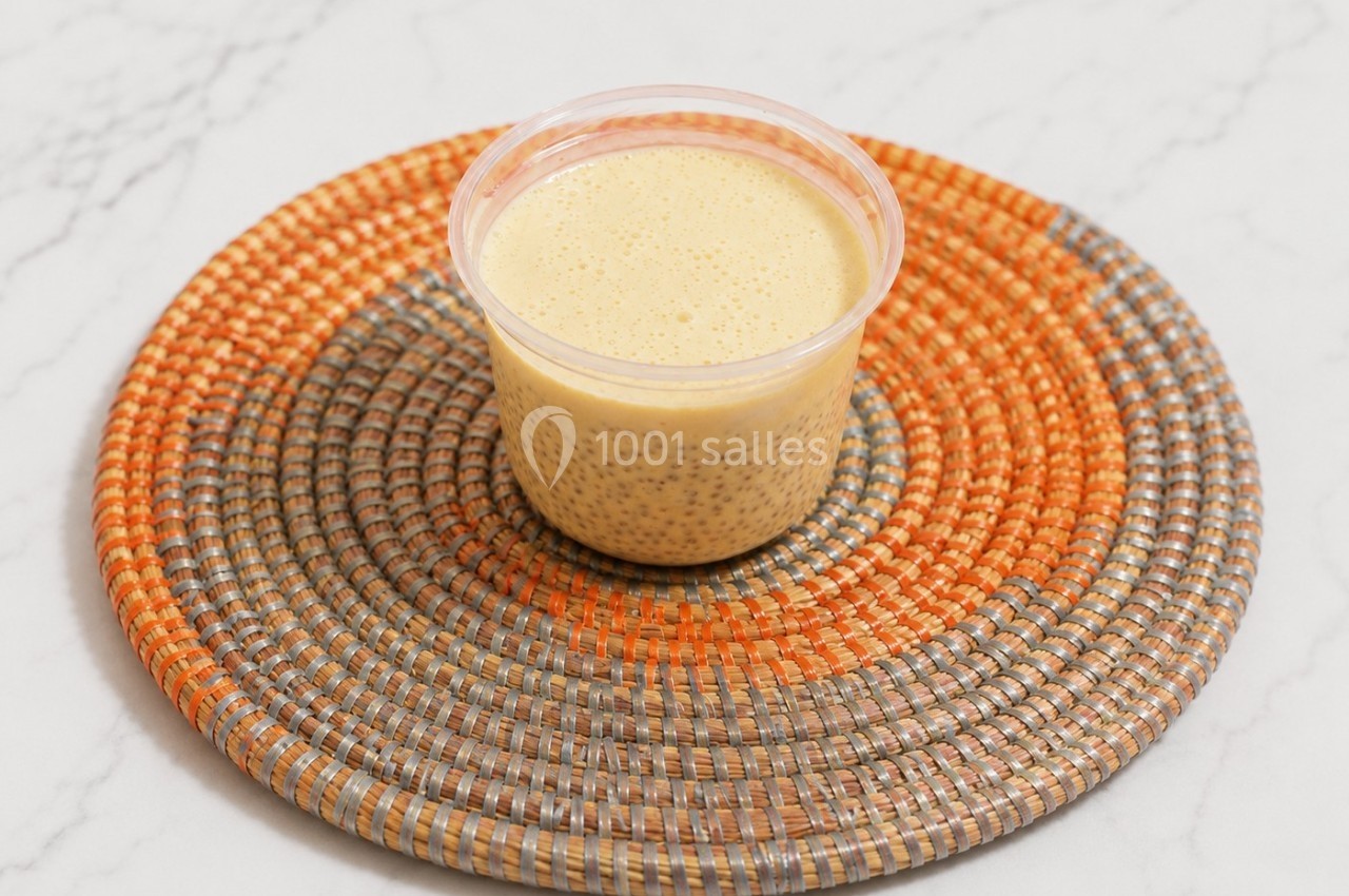 Pot de pudding au chia et lait, posé sur un dessous de plat tressé orange et gris, sur une surface en marbre.