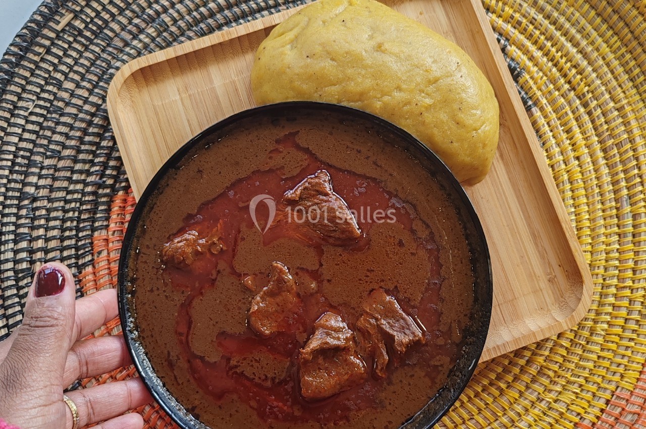 Assiette de ragoût rouge avec morceaux de viande, accompagnée d'une boule de pâte jaune sur un plateau en bois.