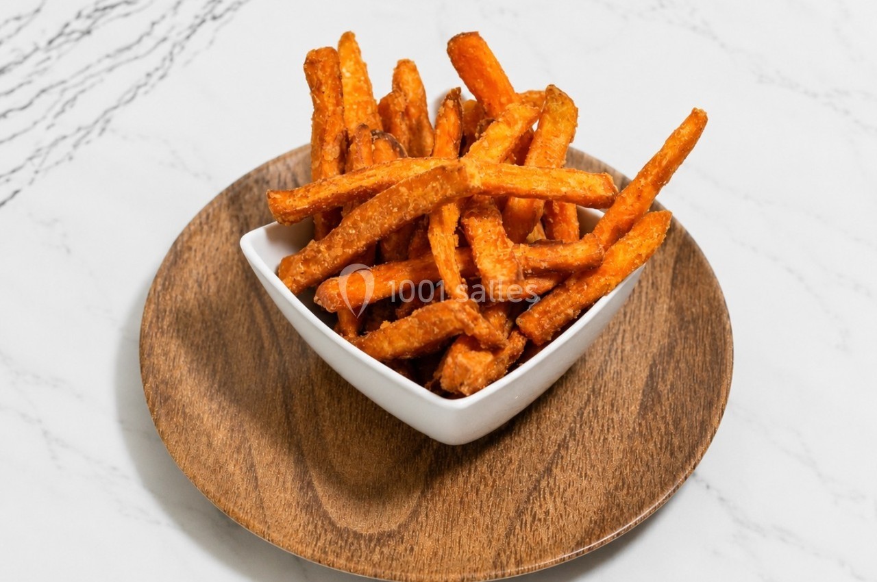 Frites de patate douce servies dans un bol blanc sur une assiette en bois, posée sur une surface en marbre.