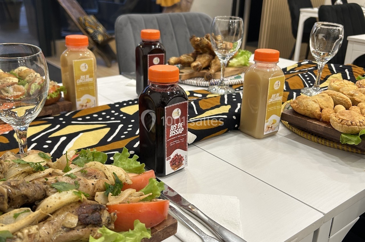 Repas dressé sur une table avec jus de bissap, pâtisseries, légumes et viandes grillées, décor africain en arrière-plan.
