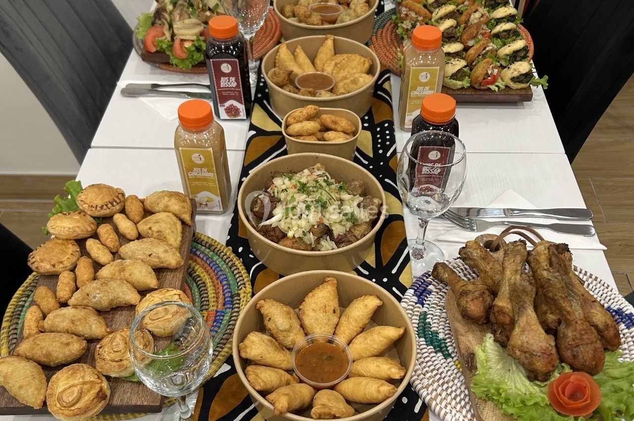 Table garnie de plats variés : empanadas, pilons de poulet, salades, sauces et jus de fruits en bouteilles.