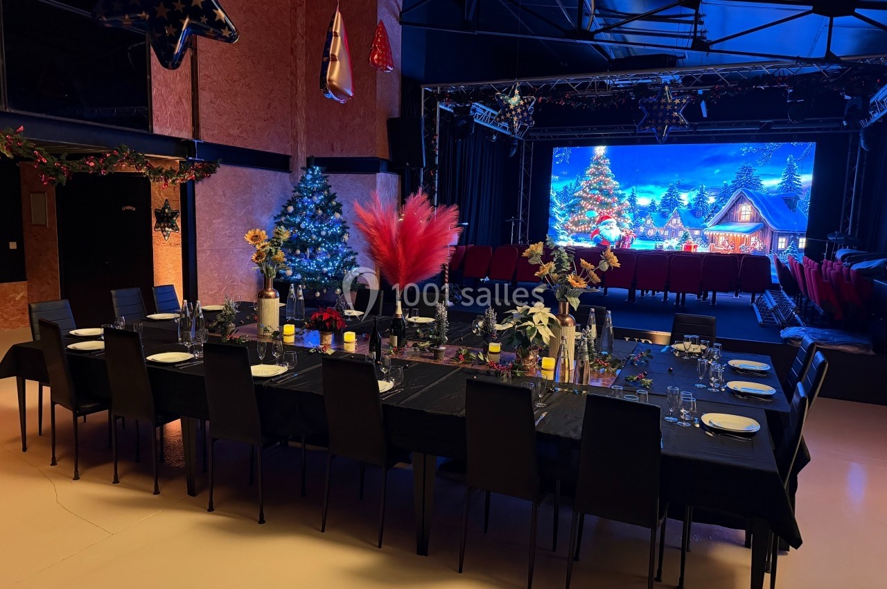 Table dressée pour un repas festif dans une salle décorée avec des guirlandes, sapins de Noël et scène illuminée.