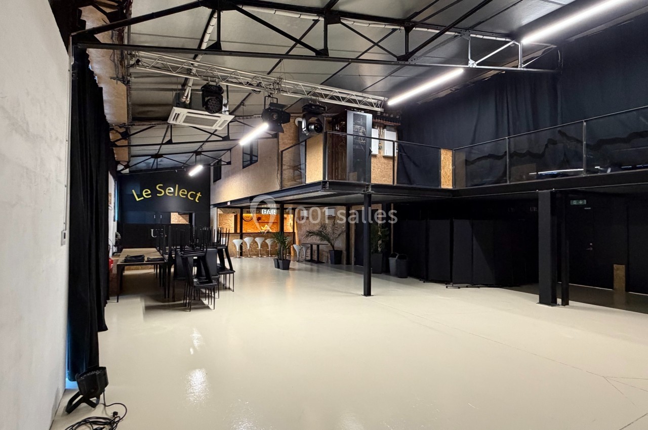 Salle moderne avec mezzanine, éclairage industriel, bar en bois et espace ouvert au sol clair.