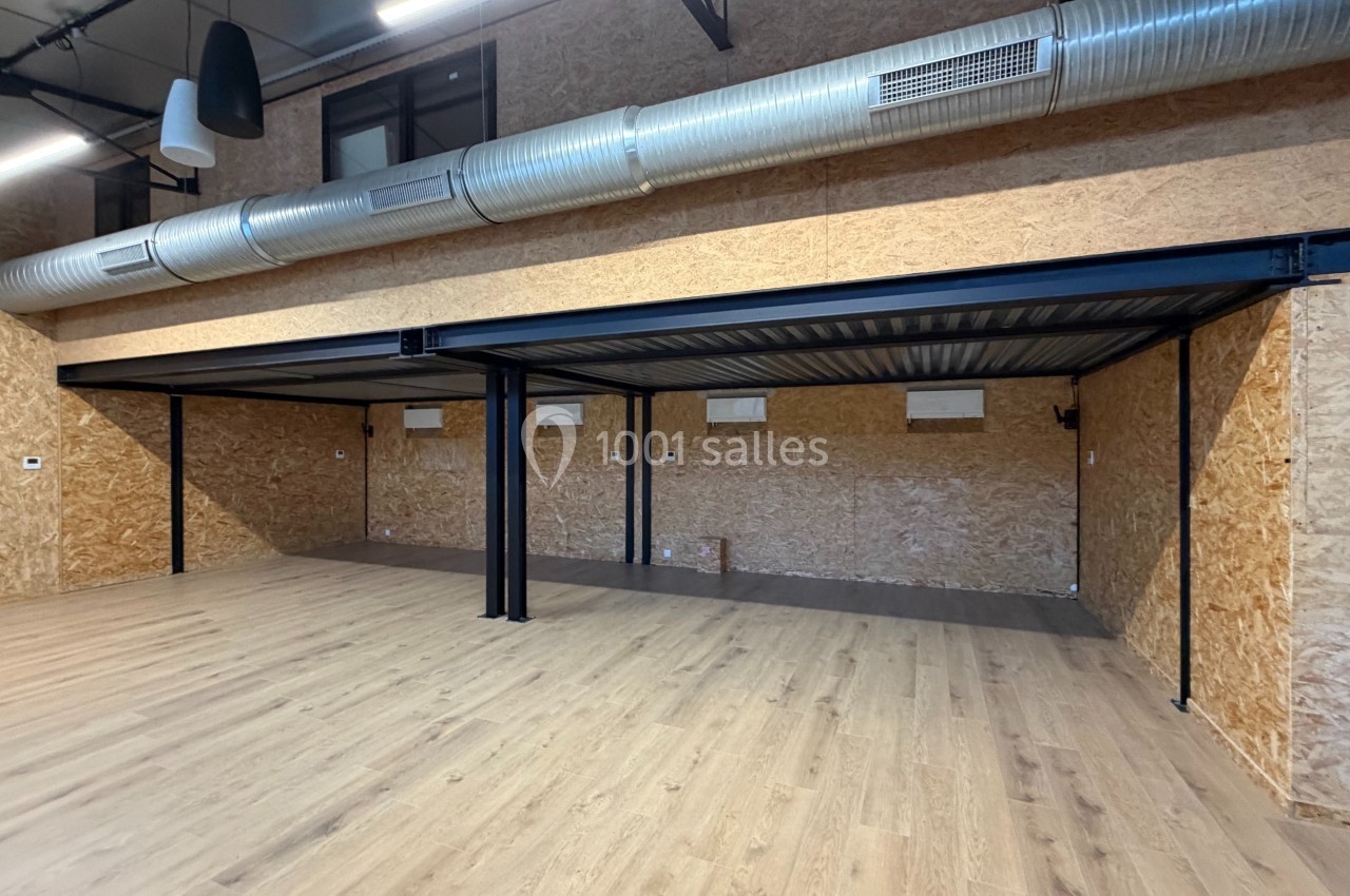 Structure métallique avec mezzanine dans un espace intérieur aux murs en bois et sol en parquet clair.