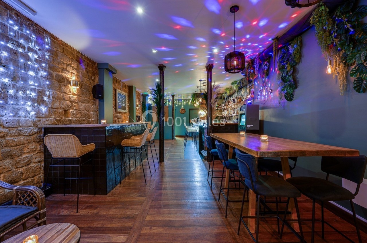 Intérieur d'un bar avec murs en pierre, éclairage tamisé, plantes suspendues et mobilier en bois et métal.