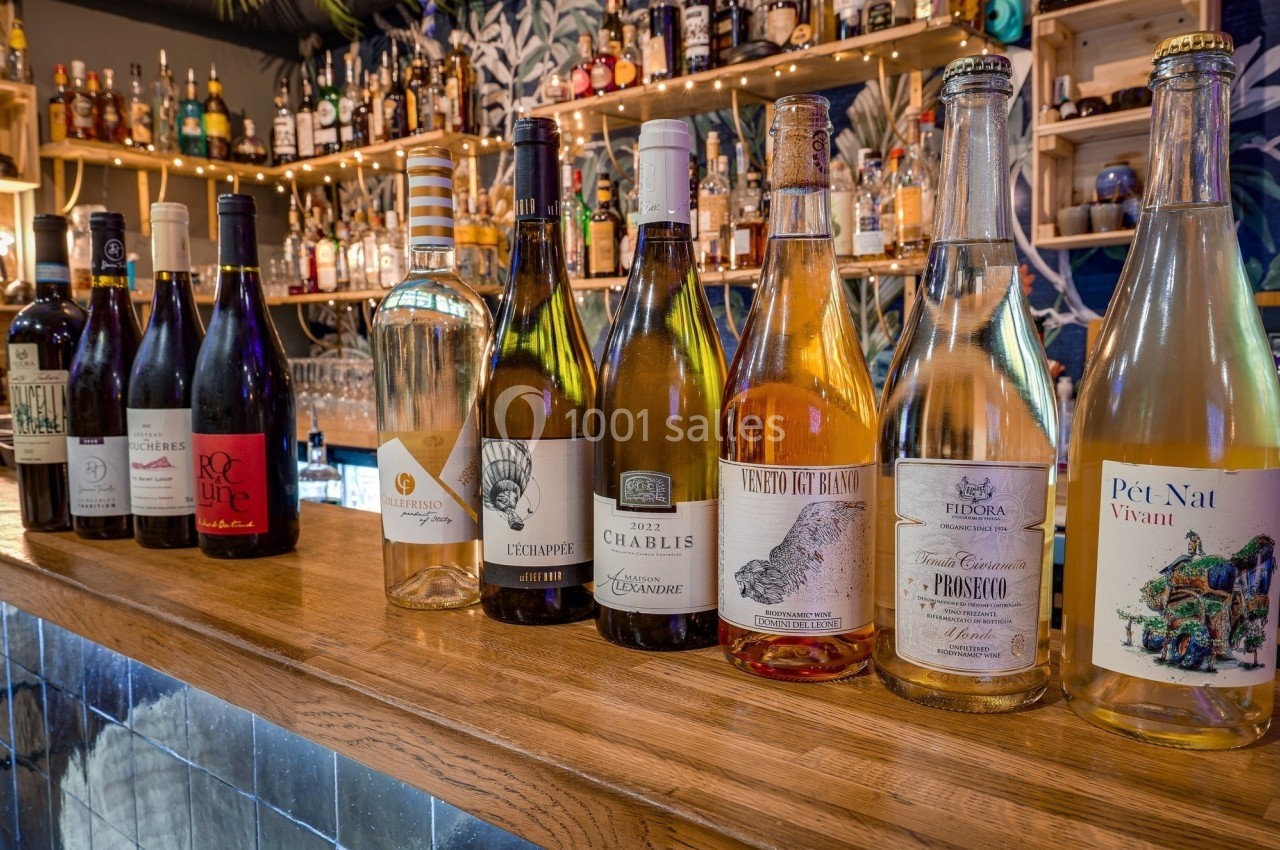 Bouteilles de vin variées alignées sur un comptoir en bois, avec un fond de bar décoré et éclairé.