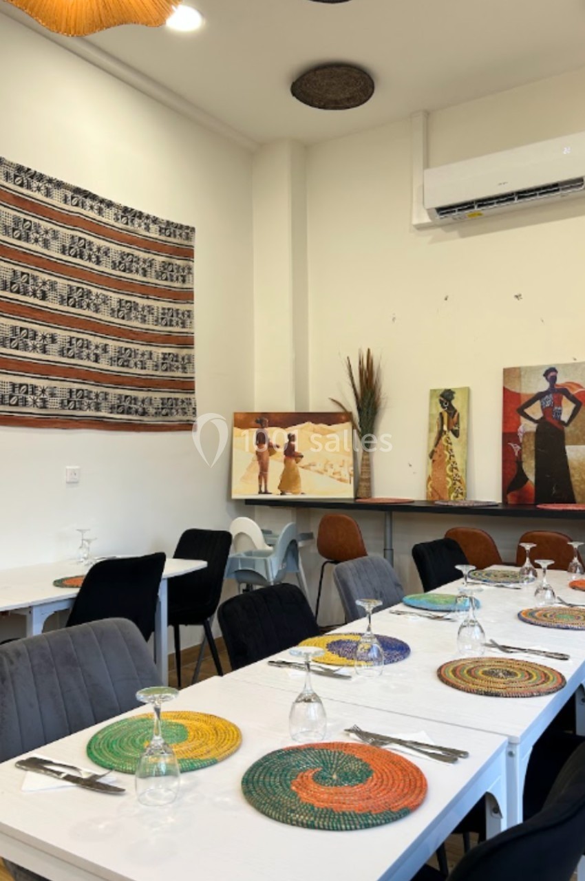 Salle de restaurant décorée avec des œuvres d'art africaines, des tables dressées et des sets de table colorés.