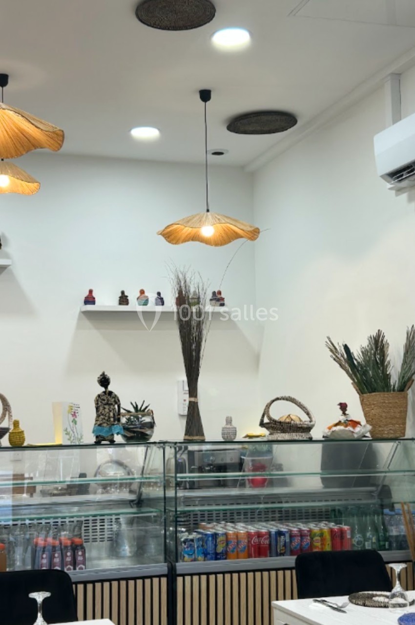 Intérieur d'un restaurant avec comptoir réfrigéré, décorations artisanales et luminaires suspendus en osier.