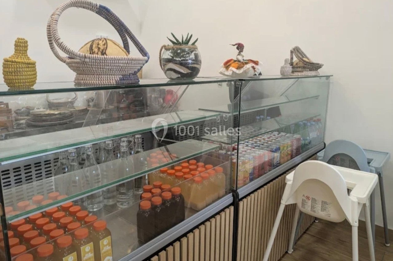 Vitrine réfrigérée contenant des boissons et des jus, avec des objets décoratifs posés sur le dessus et une chaise haute à…
