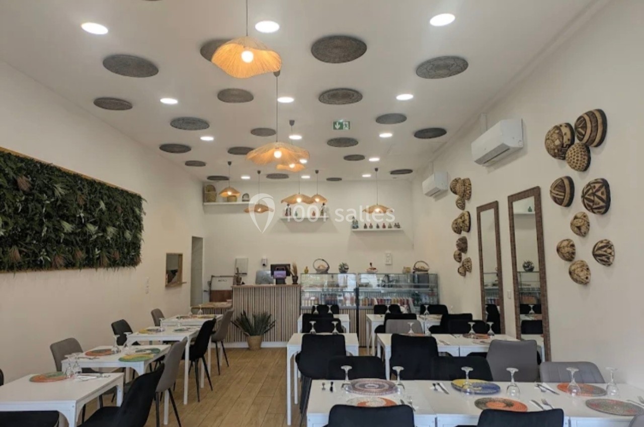 Salle de restaurant lumineuse avec décoration murale en paniers et plantes, tables dressées et comptoir au fond.