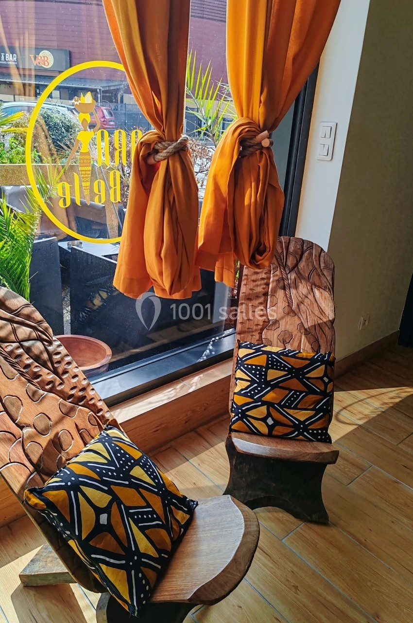 Deux chaises en bois avec coussins colorés près d'une fenêtre, rideaux orange noués et vue sur une terrasse.