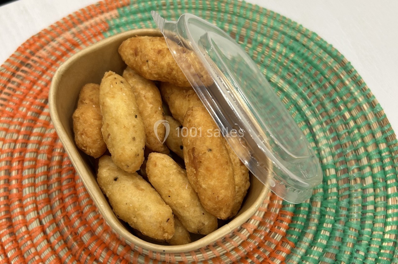 Boîte en carton contenant des beignets dorés, posée sur un dessous de plat tressé coloré.