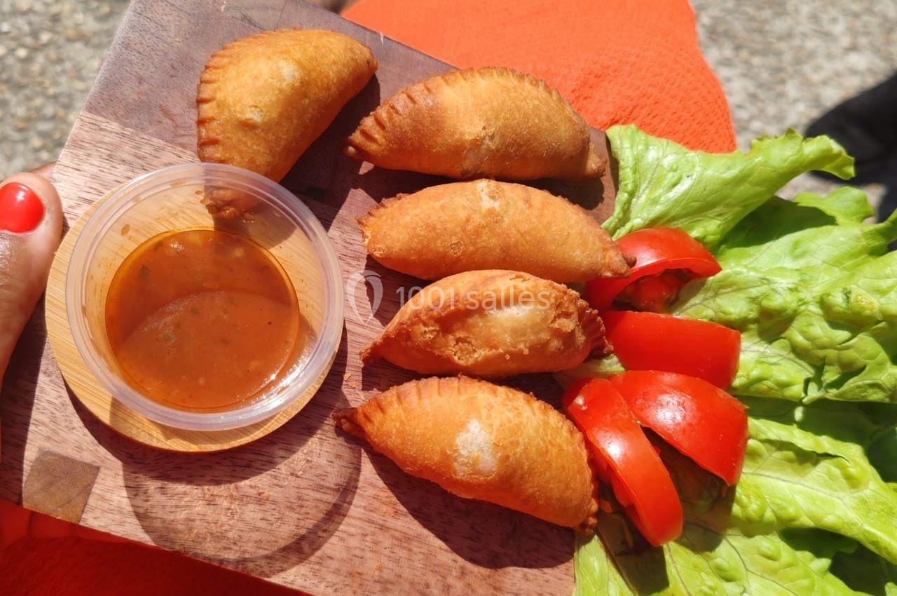 Assiette en bois avec des beignets dorés, sauce dans un récipient en plastique, laitue et tranches de tomate.