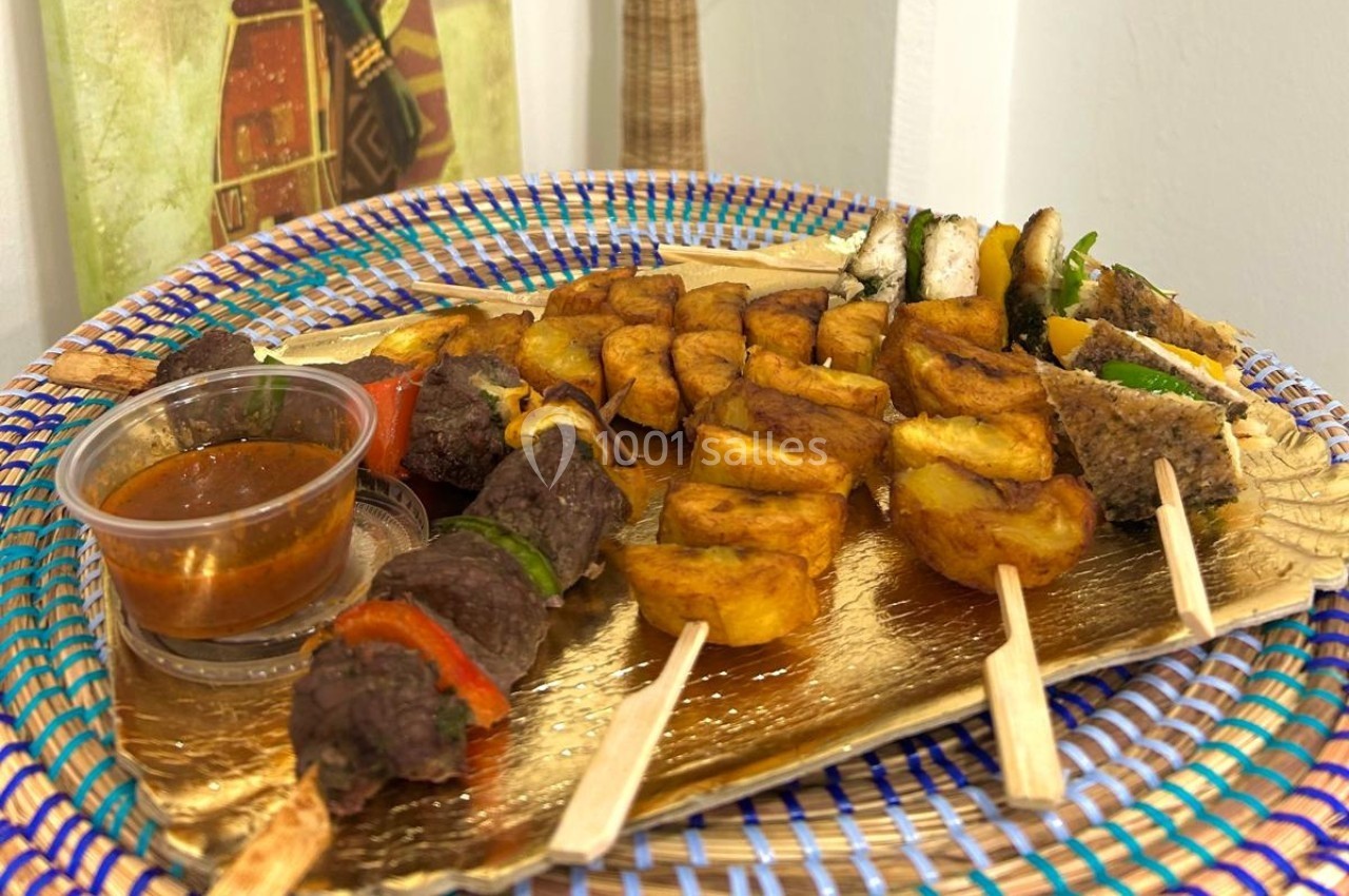 Assortiment de brochettes de viande, légumes et pommes de terre, accompagné d'une sauce, présenté sur un plateau doré.