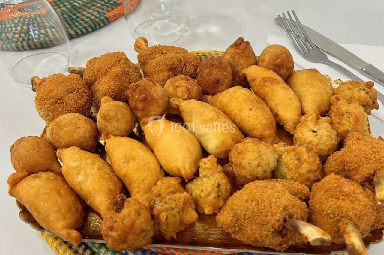 Assortiment de beignets et bouchées panées disposés sur un plateau en bois, avec des couverts en arrière-plan.