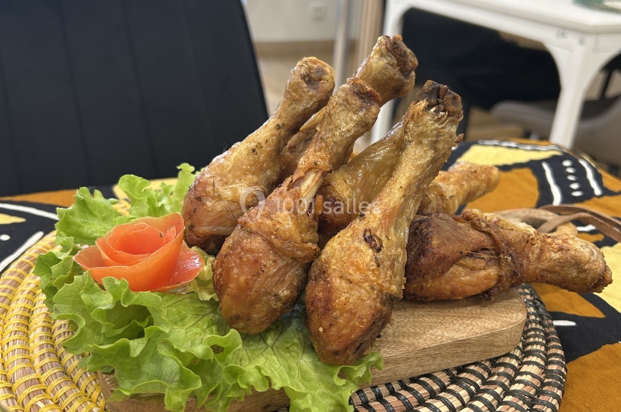Pilons de poulet rôtis disposés sur un lit de salade verte avec une décoration en forme de rose en tomate.