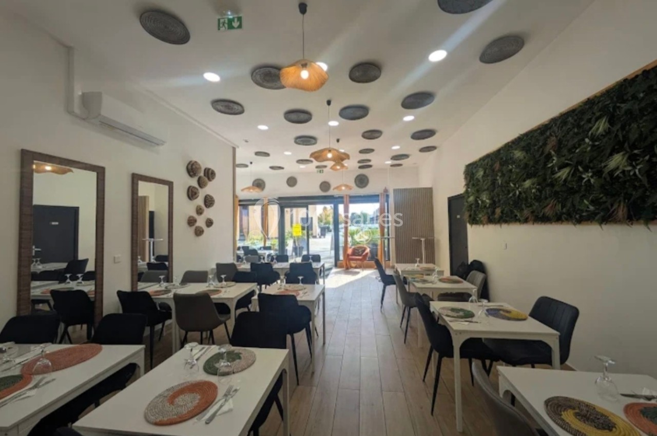 Salle de restaurant moderne avec tables dressées, décoration murale végétale et grandes baies vitrées donnant sur l…