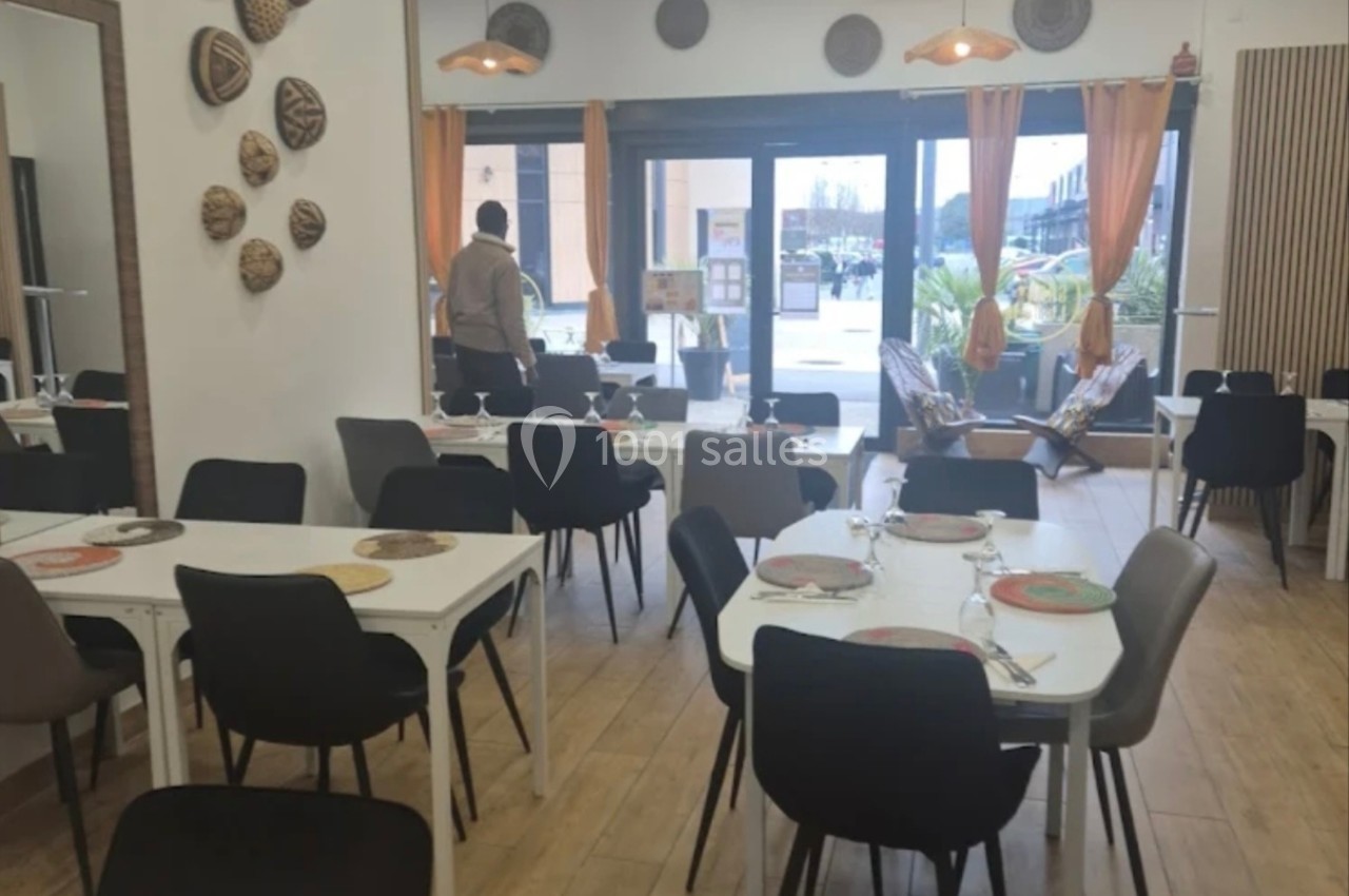 Salle de restaurant lumineuse avec tables dressées, chaises noires et blanches, et grandes baies vitrées donnant sur l…