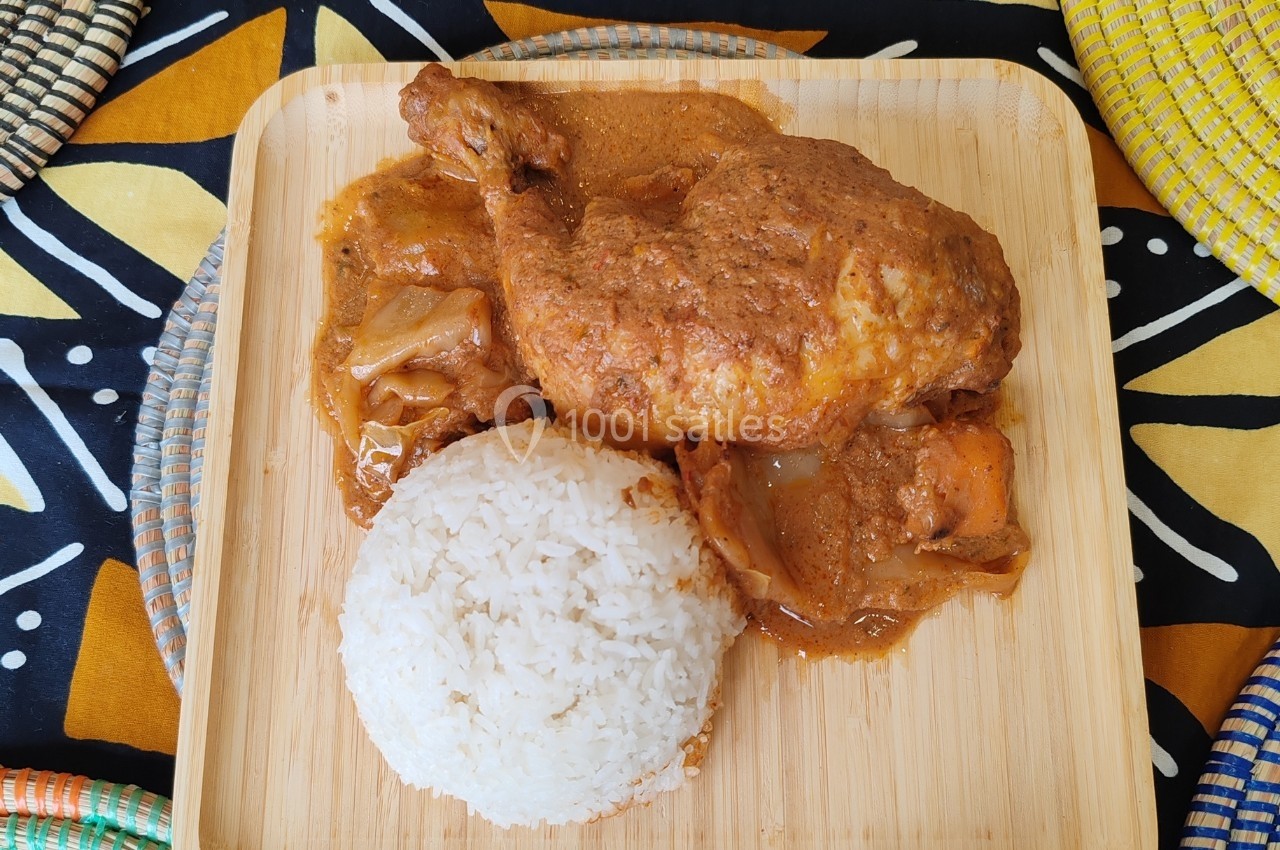 Plat de poulet mijoté en sauce avec des légumes, accompagné d'une portion de riz blanc sur une assiette en bois.