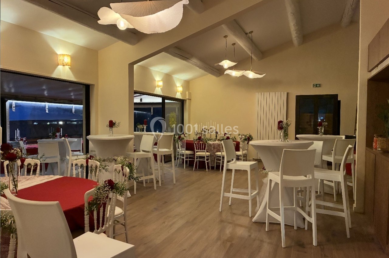 Salle de réception décorée avec des tables hautes et basses, nappes rouges, fleurs et éclairage chaleureux.