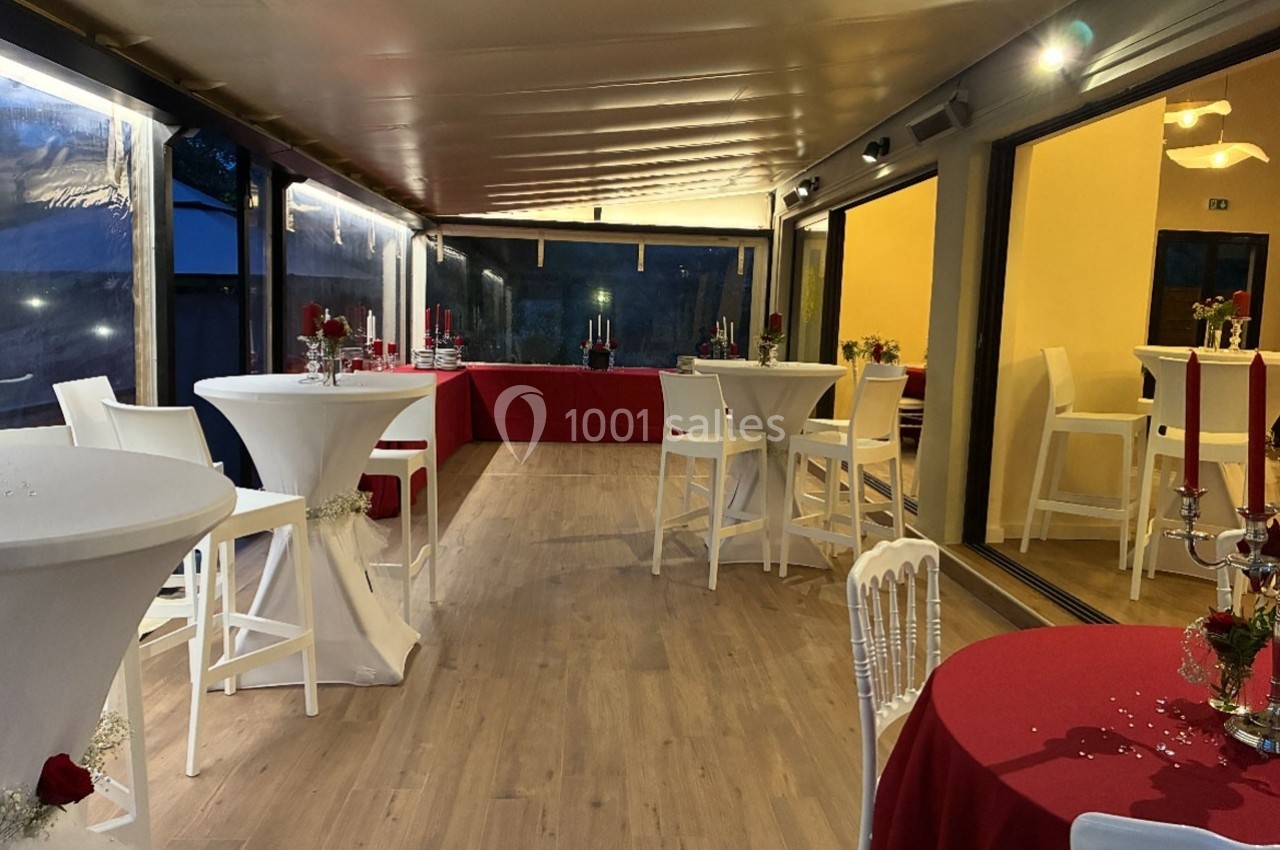 Salle aménagée avec des tables hautes et basses, nappes rouges et blanches, éclairage chaleureux en soirée.
