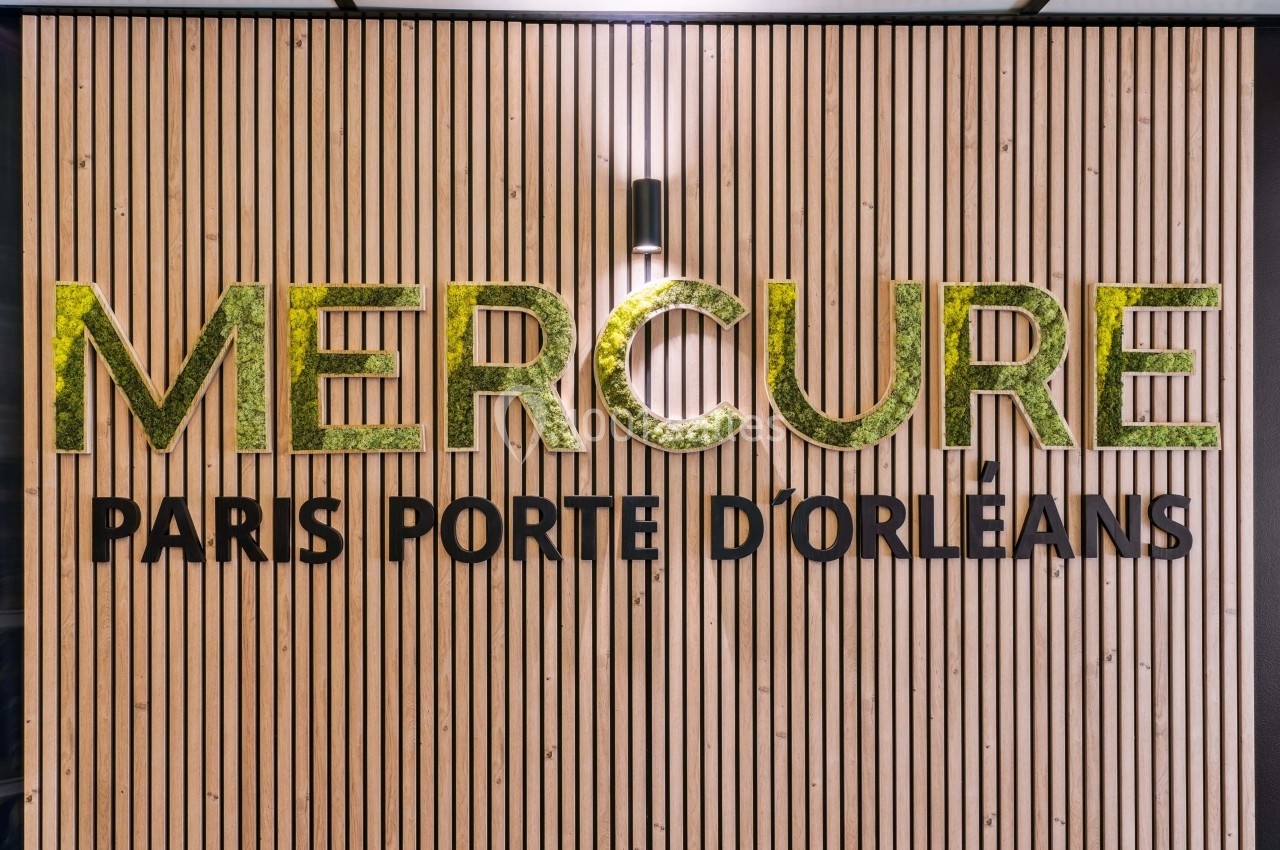 Mur en bois avec le logo ’Mercure Paris Porte d'Orléans’ en lettres dorées et éclairage intégré.