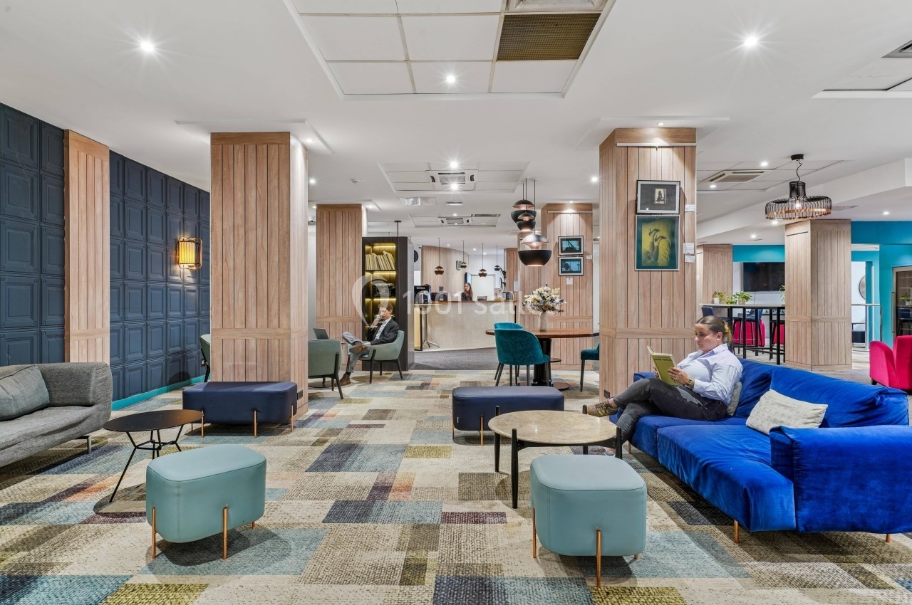 Espace lounge moderne avec canapés colorés, tables basses et personnes assises dans un décor lumineux et accueillant.