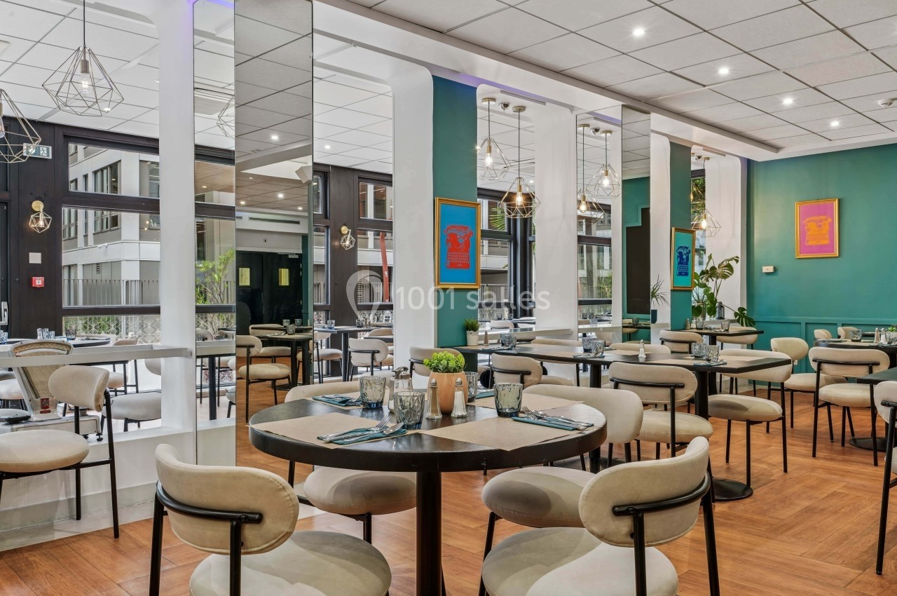 Salle de restaurant moderne avec tables dressées, chaises beige clair, murs verts et grandes baies vitrées.