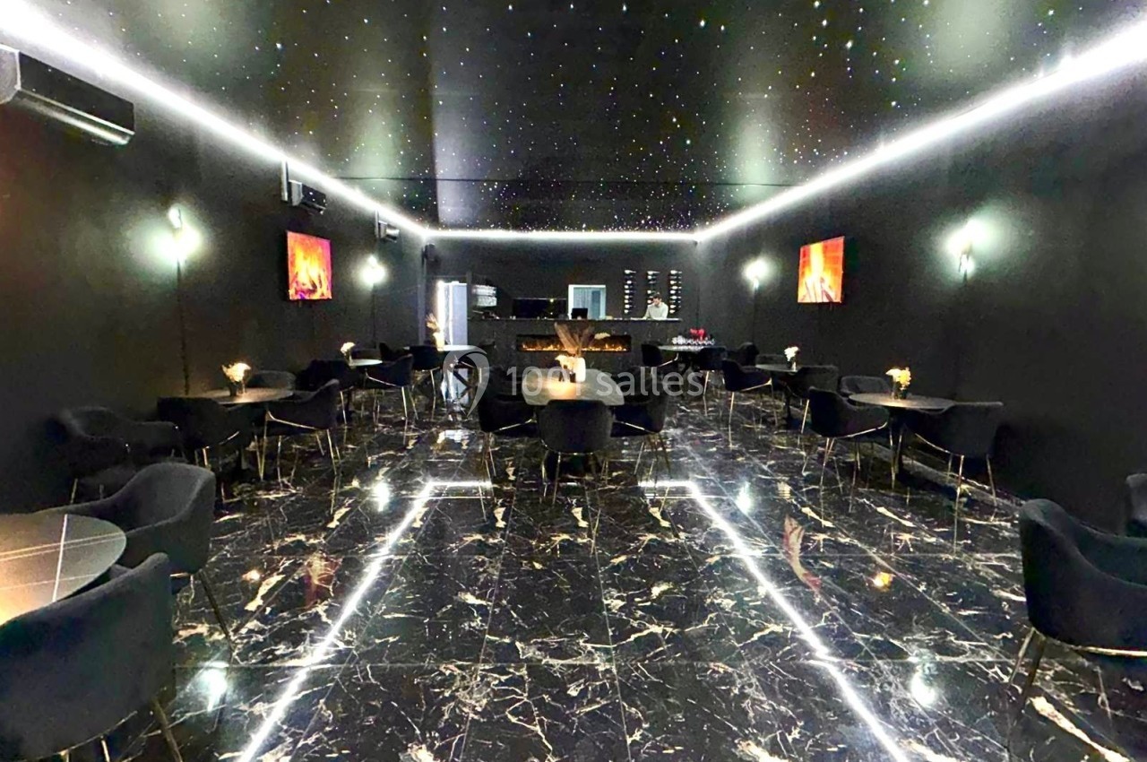 Salle moderne avec sol en marbre noir, plafond étoilé, tables rondes et éclairage tamisé.