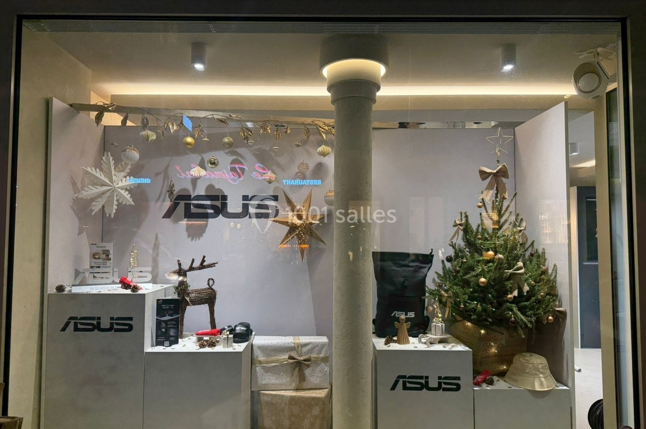 Vitrine décorée pour Noël avec un sapin, des ornements dorés et des produits Asus exposés sur des présentoirs blancs.