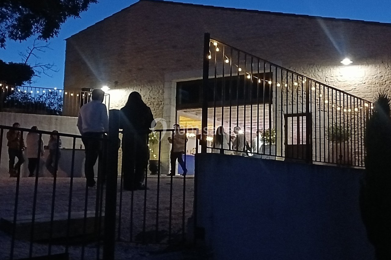 Personnes rassemblées devant un bâtiment en soirée, éclairé par des guirlandes lumineuses et entouré d'une clôture.
