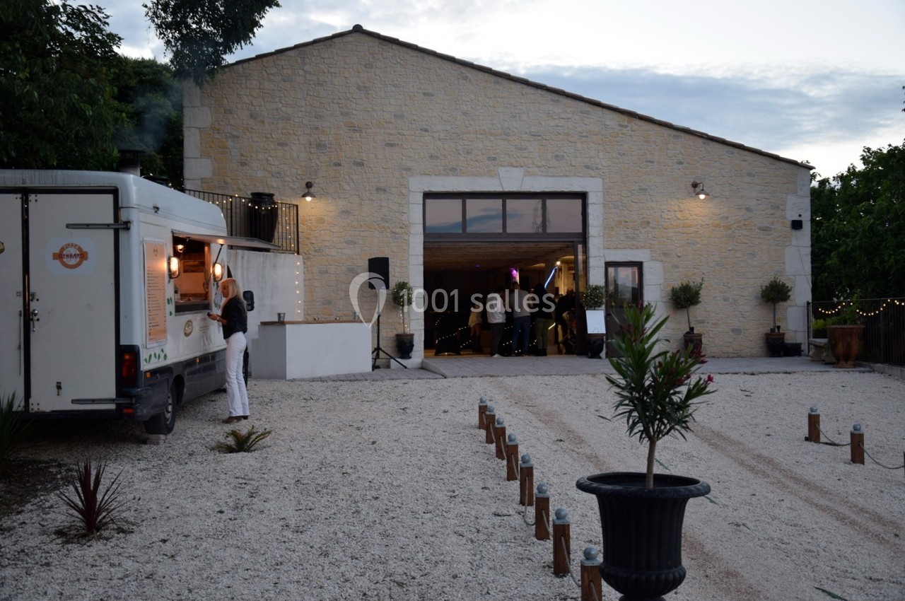 Cour extérieure d'une bâtisse en pierre avec un food truck à gauche et des personnes près de l'entrée éclairée.