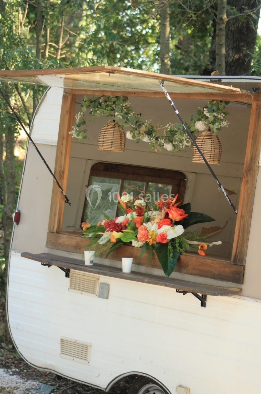 Un comptoir ouvert d'une caravane vintage décorée de fleurs colorées et de guirlandes végétales suspendues.