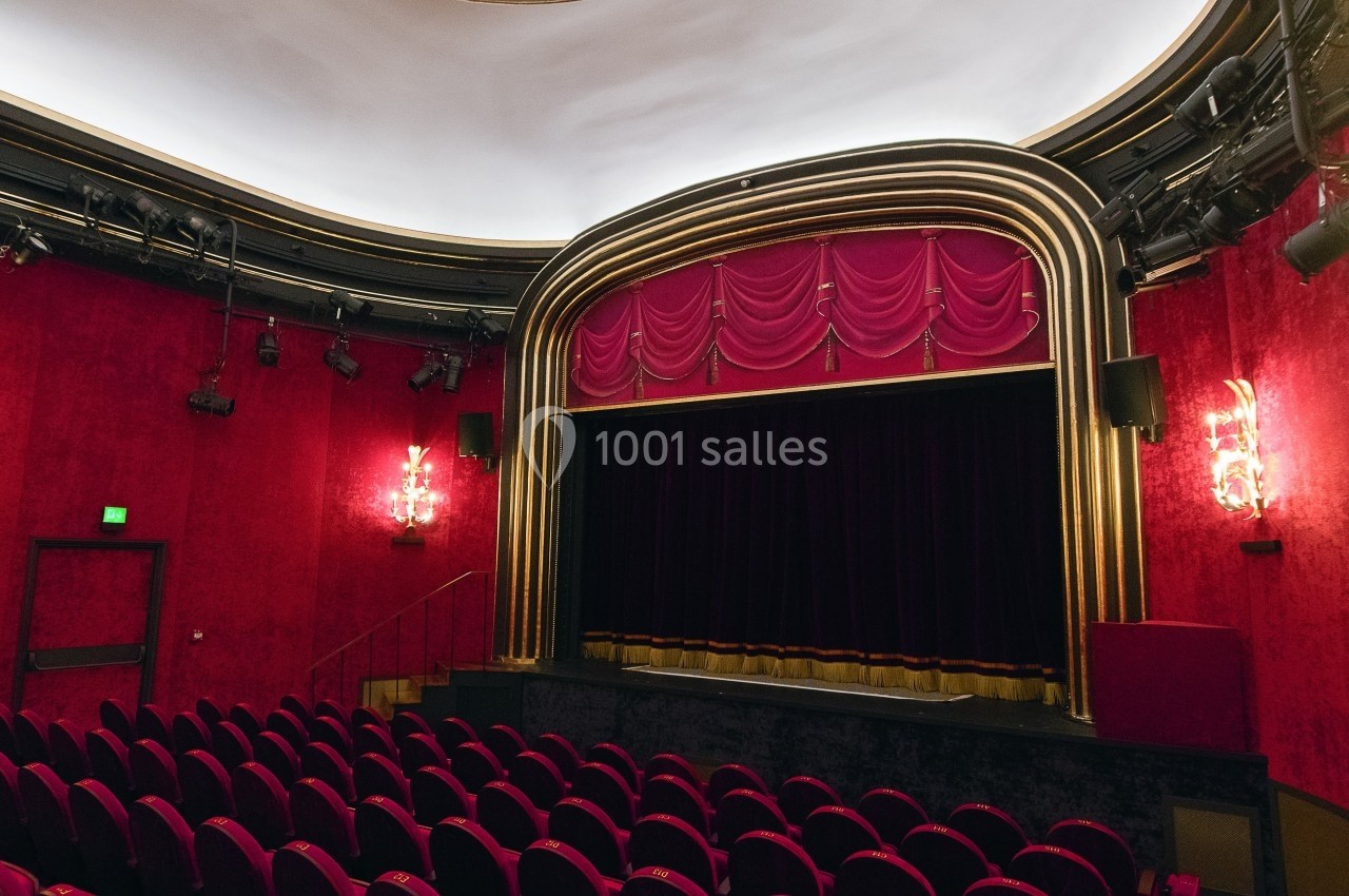 Salle de théâtre avec rideaux rouges, sièges alignés et éclairage tamisé sous un plafond arrondi.