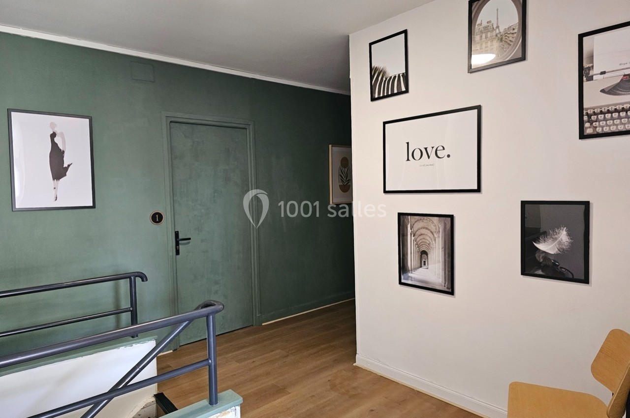 Mur décoré de cadres variés dans un intérieur moderne, avec une porte verte et un escalier au premier plan.