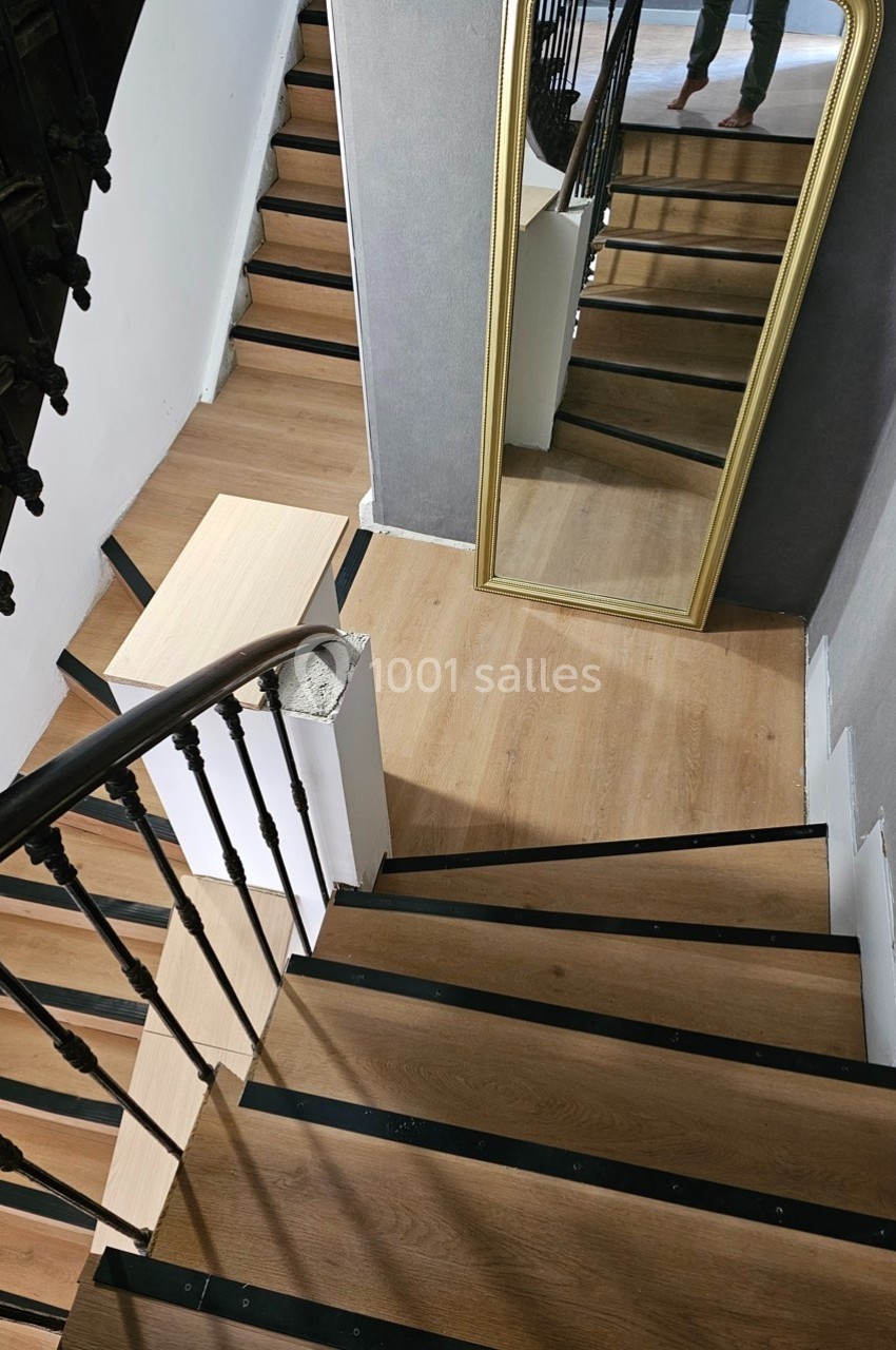 Escalier en bois avec rampe métallique, miroir doré appuyé contre un mur gris dans un espace intérieur.