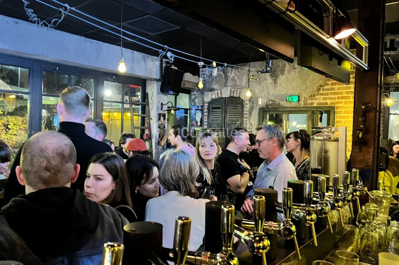 Des personnes discutent et socialisent dans un bar animé, avec des tireuses à bière au premier plan.