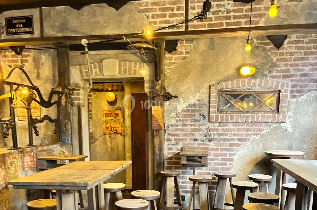 Intérieur d'un bar rustique avec murs en briques, tables en bois, tabourets et éclairage chaleureux.