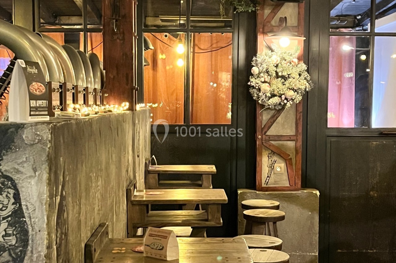 Intérieur d'un bar chaleureux avec des tables en bois, une décoration lumineuse et une couronne de Noël accrochée au mur.