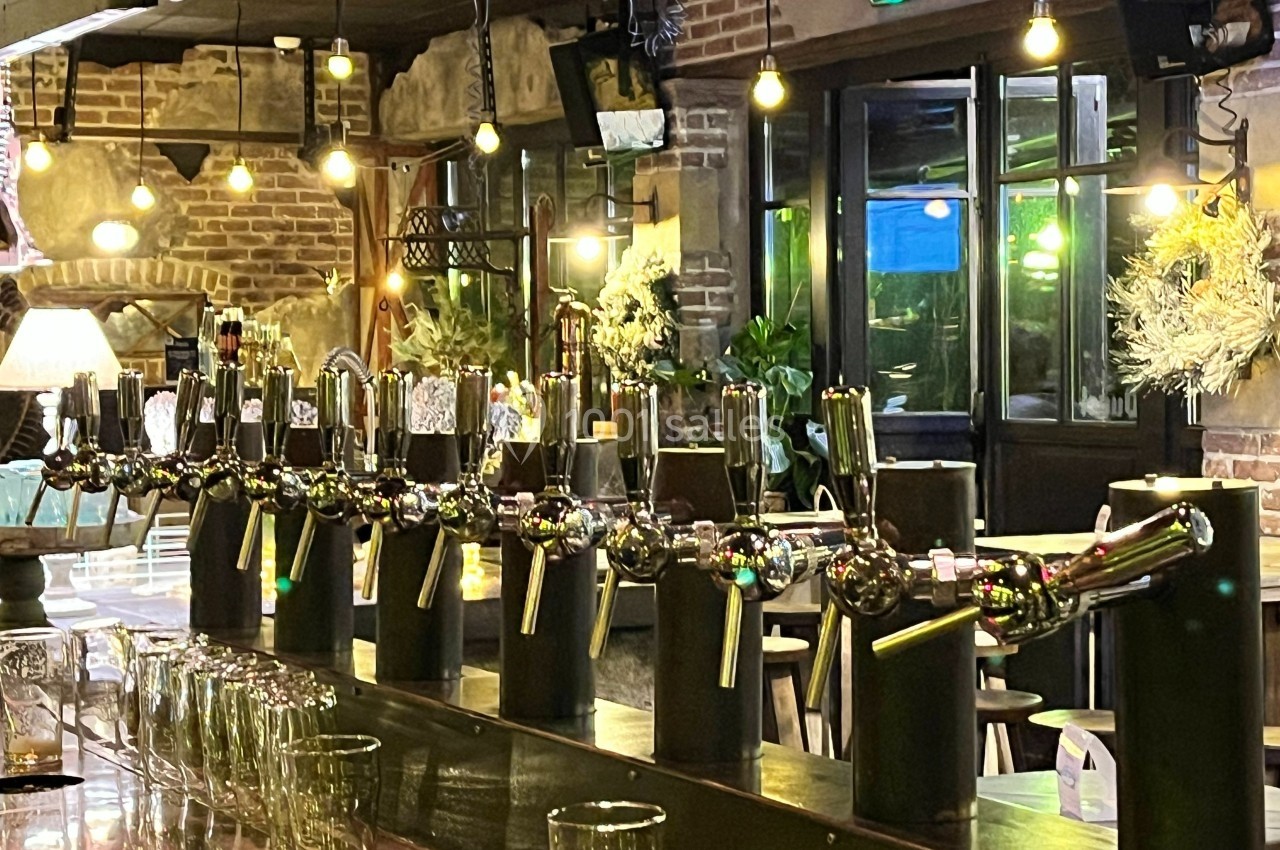Rangée de tireuses à bière alignées sur un comptoir en bois dans un bar à l'ambiance chaleureuse et lumineuse.
