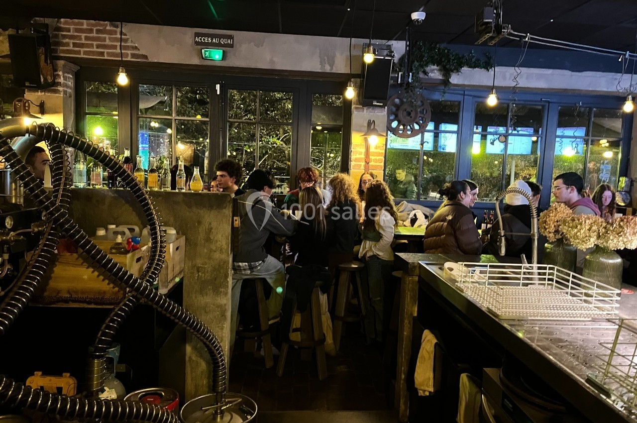 Des personnes assises à un bar dans une ambiance chaleureuse avec des lumières tamisées et une grande baie vitrée.