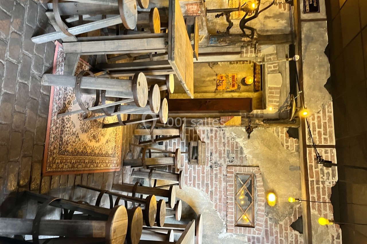 Salle rustique avec murs en briques, mobilier en bois brut, tapis au sol et éclairage chaleureux suspendu.